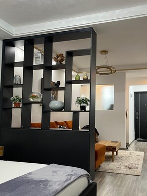 Un dormitorio moderno con cama, cabecera de madera, separador negro con estantes y una pequeña mesa con silla.