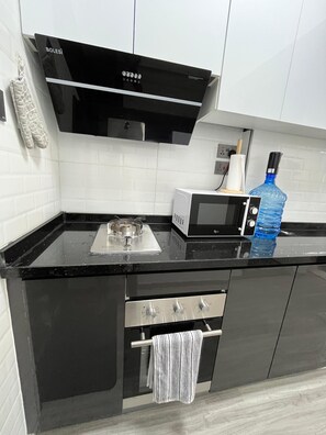 Eine Küche mit schwarzem Arbeitsplatz, einem Edelstahlbackofen, einer Mikrowelle und einer großen blauen Wasserflasche.