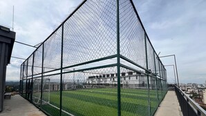 Cancha deportiva rodeada por una cerca de alambre con un camino de hormigón y una banca.