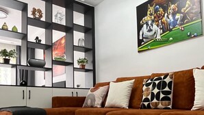 Una sala de estar moderna con un sofá marrón, una mesa de centro de madera, un estante negro con objetos decorativos y un cuadro de perros jugando al billar.
