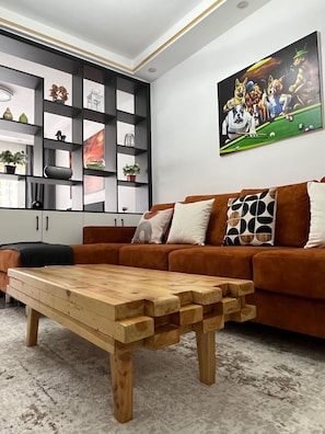 Ein modernes Wohnzimmer mit einem braunen Sofa, einem Holztisch, einer schwarzen Regaleinheit mit Dekoration und einem Gemälde von Hunden beim Billardspielen.