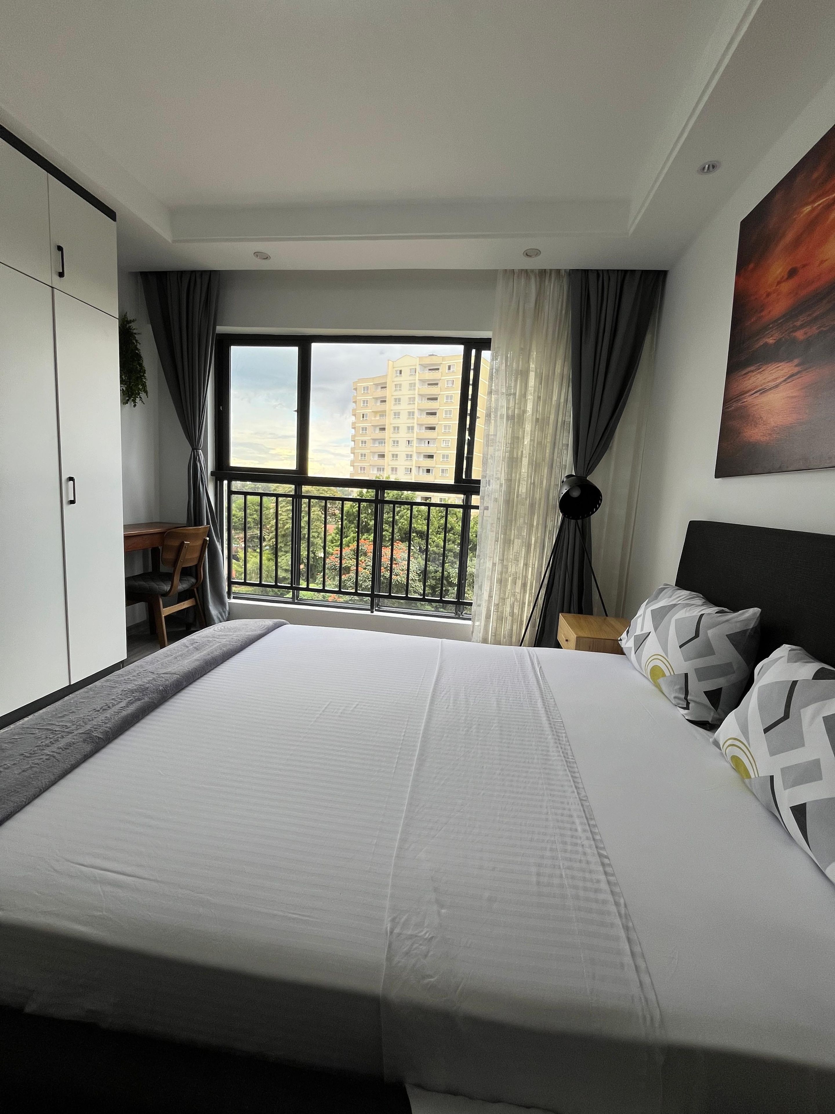 Un dormitorio con una cama grande, un escritorio y vistas a un balcón con un edificio al fondo.