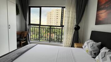 Un dormitorio con una cama grande, un escritorio y vistas a un balcón con un edificio al fondo.