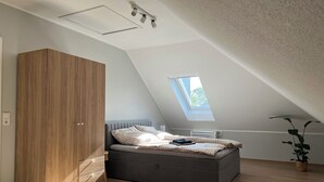 Quarto com teto inclinado, claraboia, cama, guarda-roupa e planta em vaso.