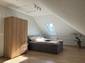 Een slaapkamer met een schuine plafond, dakraam, bed, kast en een potplant.