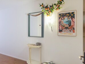Quarto com espelho, uma pequena mesa com uma tigela, luminária na parede e um quadro emoldurado.