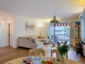 A living room with a sofa, a dining table with chairs, a vase with flowers, and a painting on the wall. - Casa Sole sul Lago by Interhome (Brissago)