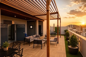 Eine Dachterrasse mit Holzboden, Sitzgelegenheiten und Blick auf die Stadt bei Sonnenuntergang.