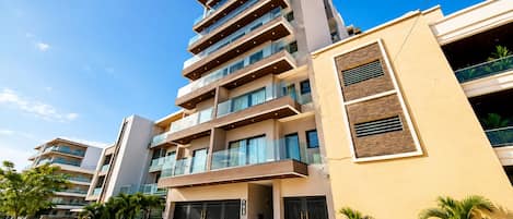 A multi-story residential building with balconies, a gated entrance, and a paved driveway.