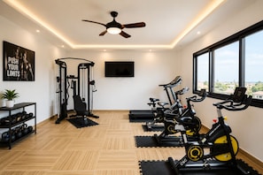 Ein Fitnessraum mit Trainingsgeräten, einem Deckenventilator und einem Fernseher an der Wand.