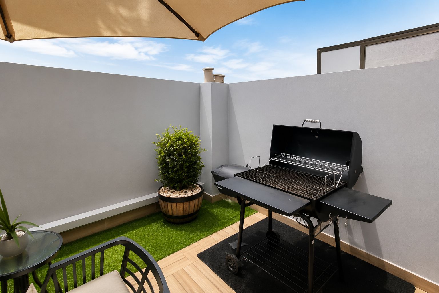 A patio with a grill, a potted plant, and a table with chairs.