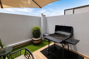 Une terrasse avec un barbecue, une plante en pot et une table avec des chaises.