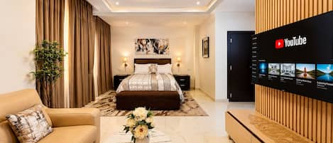 A modern hotel room with a bed, a TV mounted on the wall, a sofa, and a coffee table with a vase of flowers.