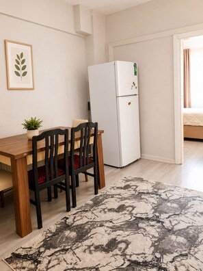 A dining area with a wooden table and chairs, a white refrigerator, a potted plant, and a patterned rug. - 3BR Istanbul Apartment In Historic Balat + Golden Horn Views (Istanbul)