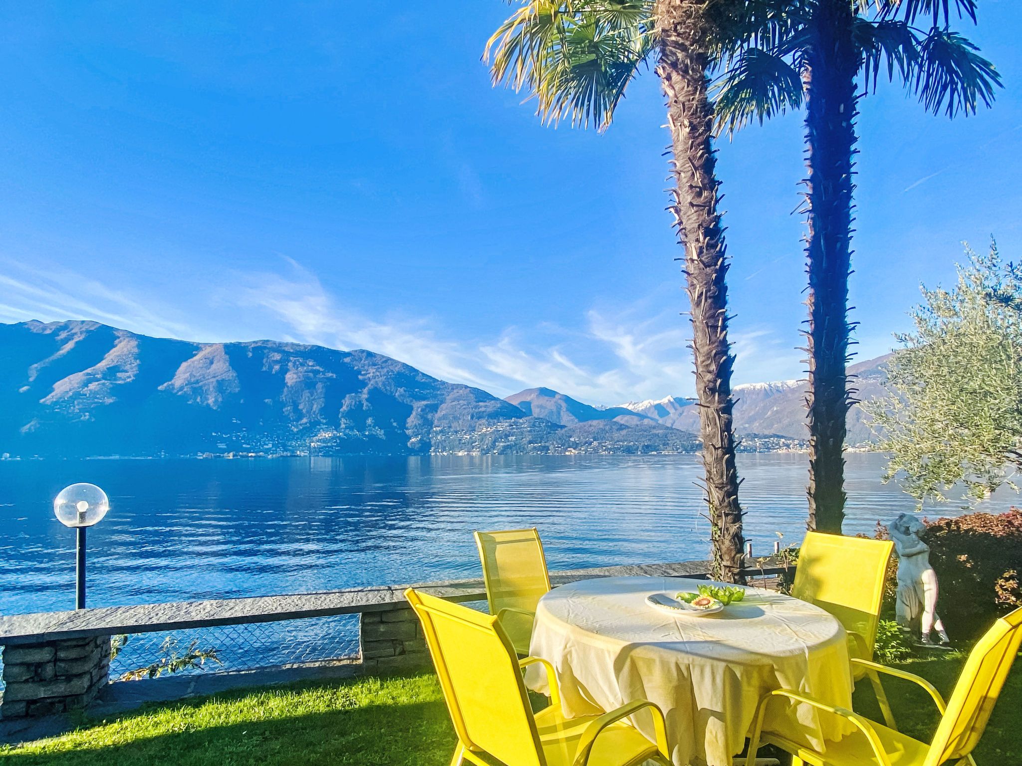 A table with yellow chairs, a clear view of a lake, and mountains in the background.