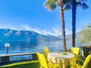 A table with yellow chairs, a clear view of a lake, and mountains in the background. - Casa Matani (Seezugang) by Interhome (Ranzo)