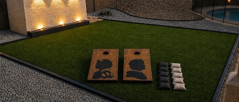 Un jardín bien cuidado con césped artificial, un muro decorativo con luces y una piscina.