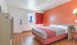 Habitación de hotel con cama, escritorio, silla, ventana con cortinas y puerta.