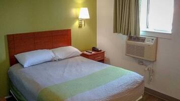 Una habitación de hotel con cama, lámpara de noche, mesita de noche y un equipo de aire acondicionado.