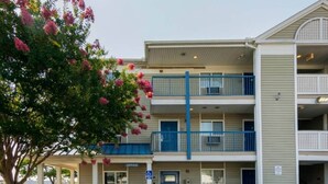 Ein mehrstöckiges Gebäude mit einem Büro im Erdgeschoss, einem blauen Geländer im zweiten Stock und einem Baum mit rosa Blüten vor der Fassade.