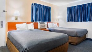 Ein Hotelzimmer mit zwei Betten, einem Holzkopfteil, einer Wand-Klimaanlage und blauen Vorhängen.