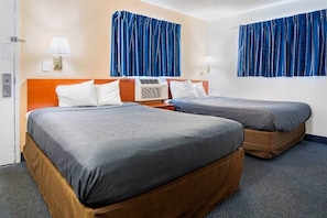 Ein Hotelzimmer mit zwei Betten, einem Holzkopfteil, einer Wand-Klimaanlage und blauen Vorhängen.