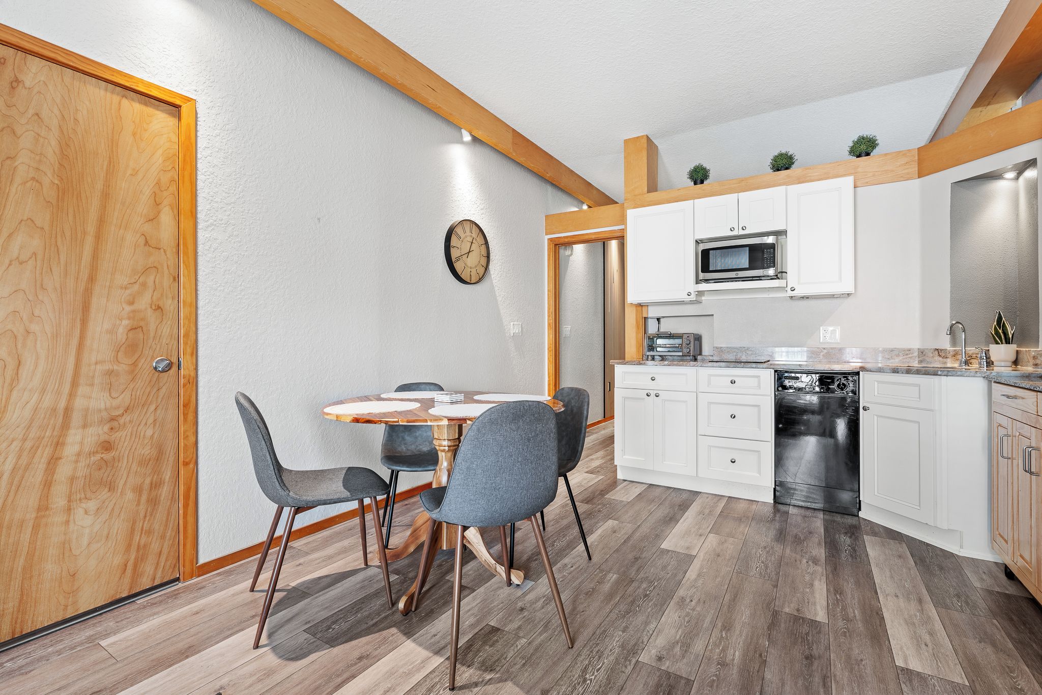 Cocina compacta con armarios blancos, microondas, tostadora y lavavajillas.