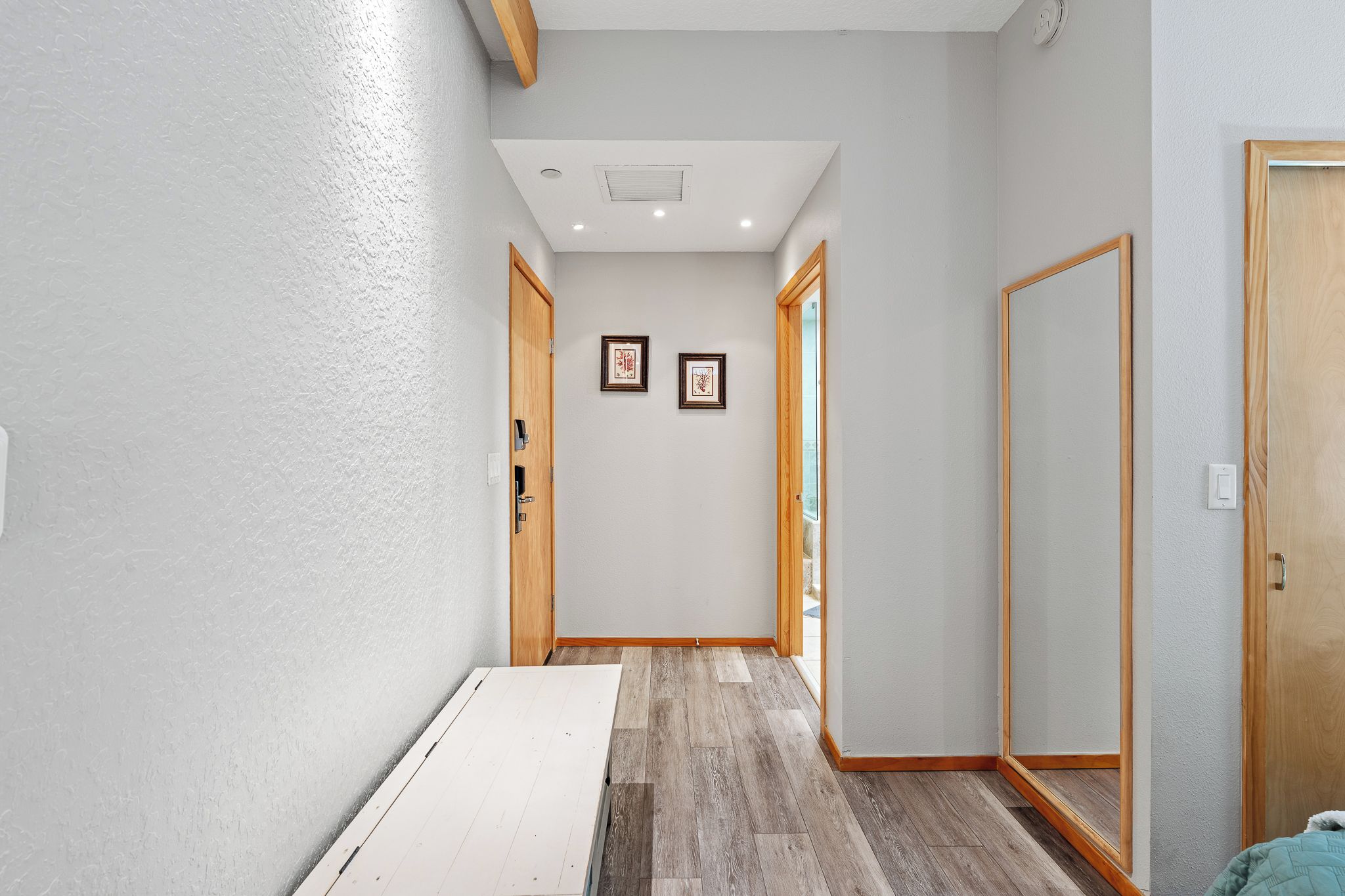 Un estrecho pasillo con puertas de madera, un radiador blanco y dos cuadros en la pared.