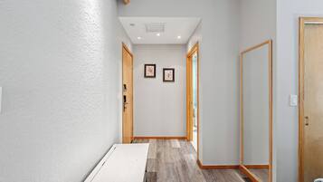 Un estrecho pasillo con puertas de madera, un radiador blanco y dos cuadros en la pared.