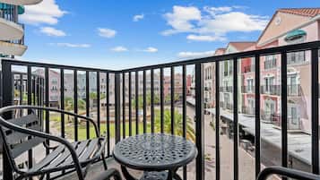 Un balcón con mesa y sillas, con vista a un patio con edificios y un cielo despejado.