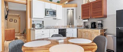 A modern kitchen with white cabinets, a microwave, a coffee maker, and a dining area with a wooden table and chairs.