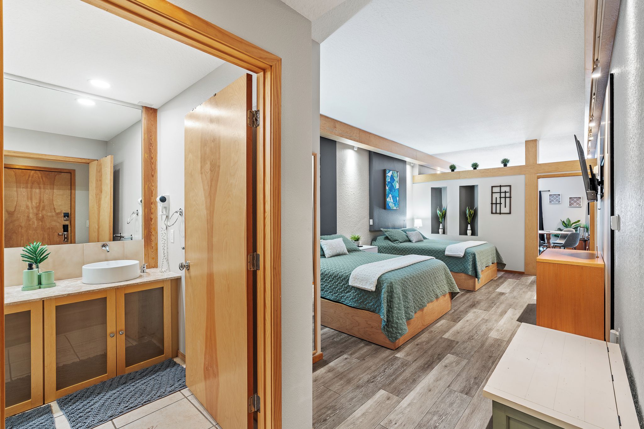 Un dormitorio moderno con dos camas, un baño con lavamanos y espejo, y una pequeña zona de escritorio.