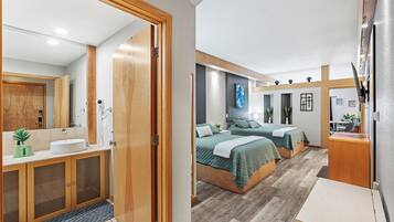 Un dormitorio moderno con dos camas, un baño con lavamanos y espejo, y una pequeña zona de escritorio.