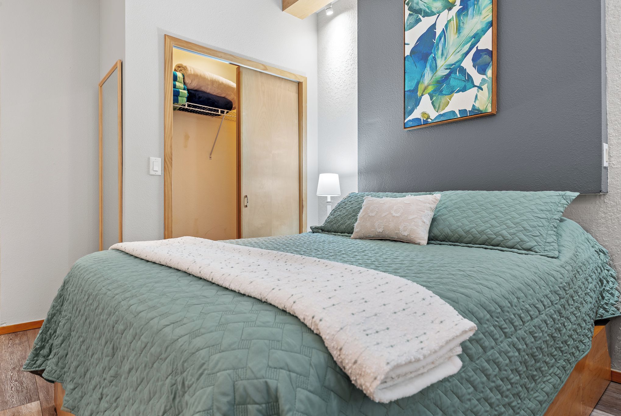A bedroom with a bed, a wardrobe, a painting, and a lamp.