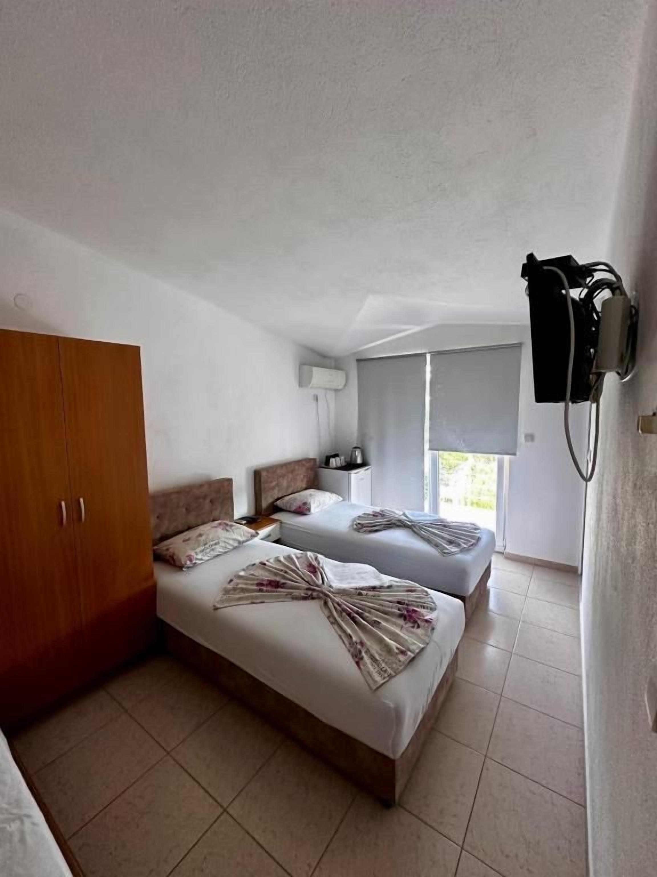 A hotel room with two beds, a wardrobe, a window, and a wall-mounted air conditioning unit.