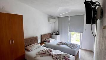 A hotel room with two beds, a wardrobe, a window, and a wall-mounted air conditioning unit.