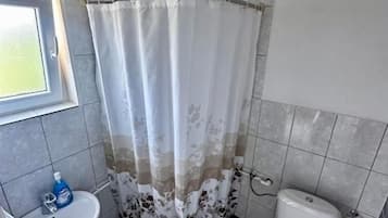 Casa de banho com cortina de chuveiro, sanita, lavatório e janela.