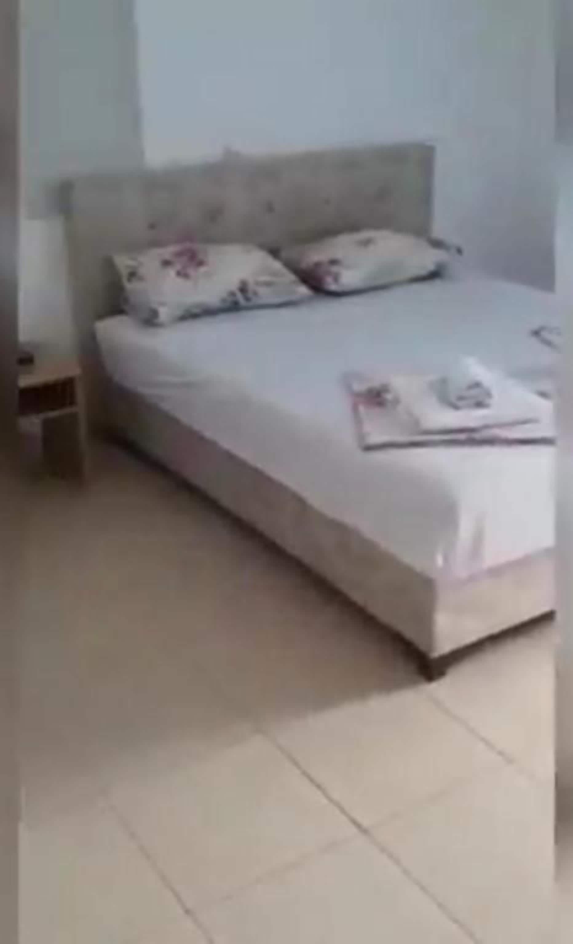 A bed with a headboard, two pillows, and a folded towel on the bed.