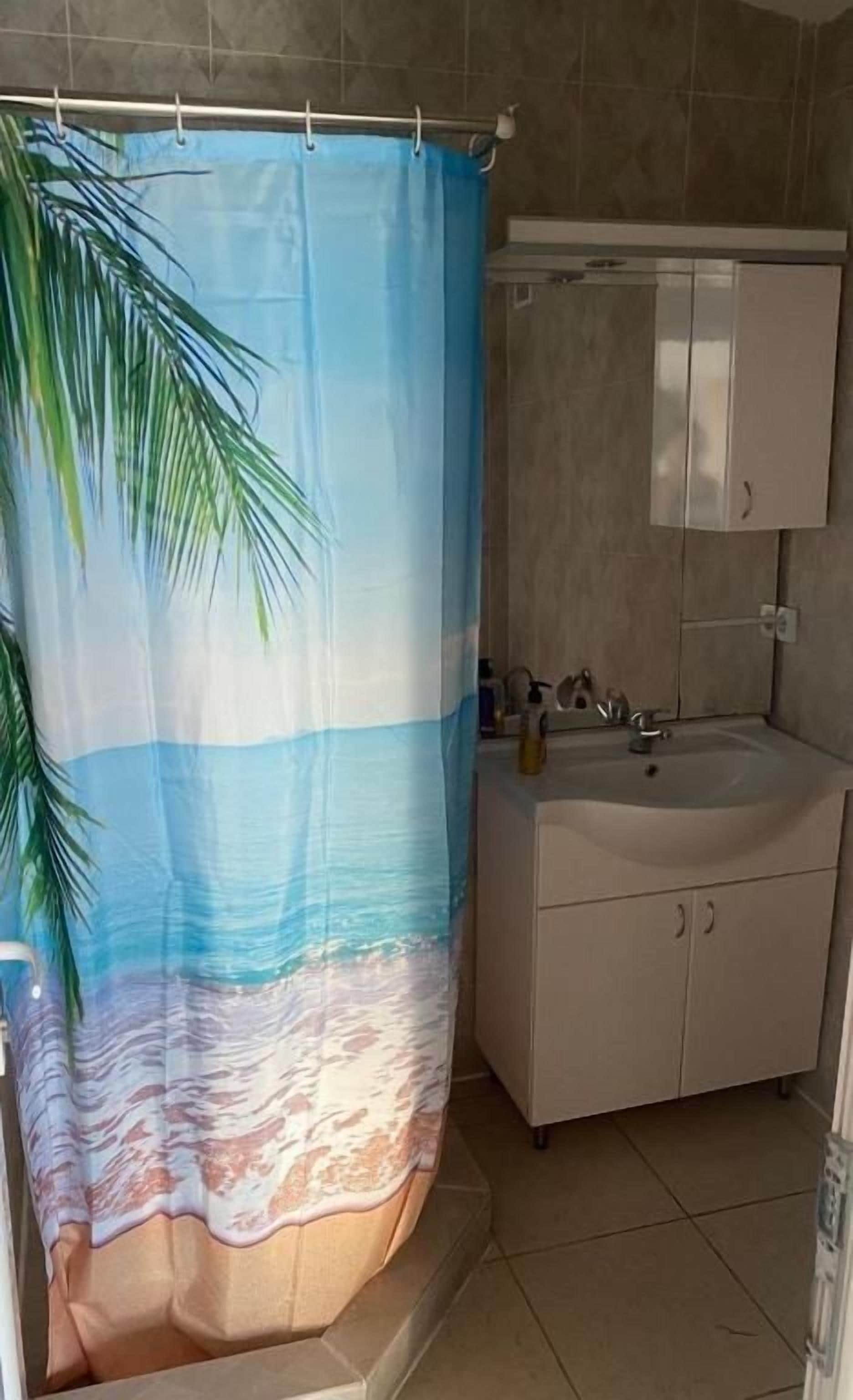 A bathroom with a shower curtain depicting a beach scene, a sink, and cabinets.