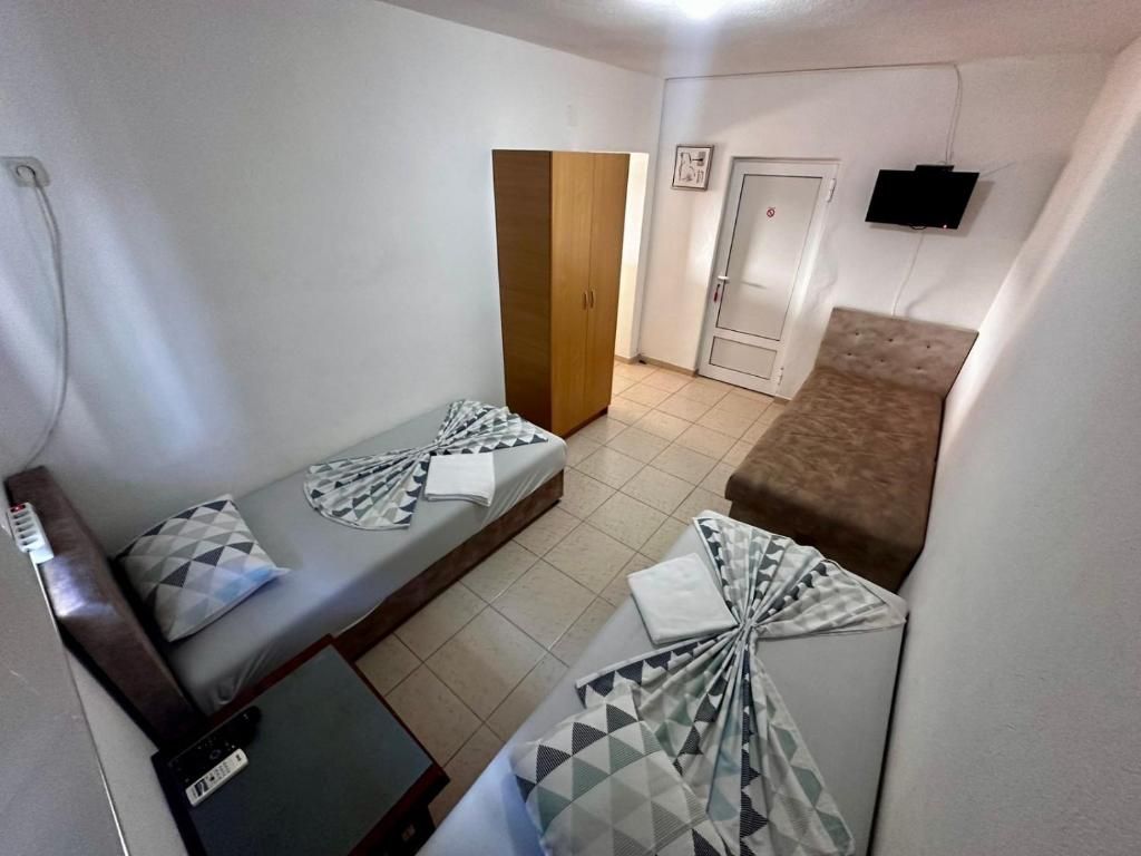 A small, compact room with two single beds, a sofa, a TV mounted on the wall, and a wardrobe.