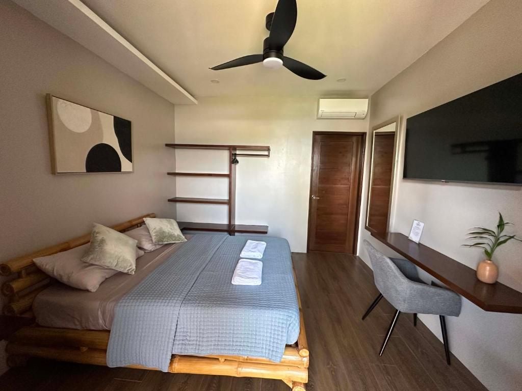 Un dormitorio con cama, escritorio, silla, ventilador de techo y un cuadro en la pared.