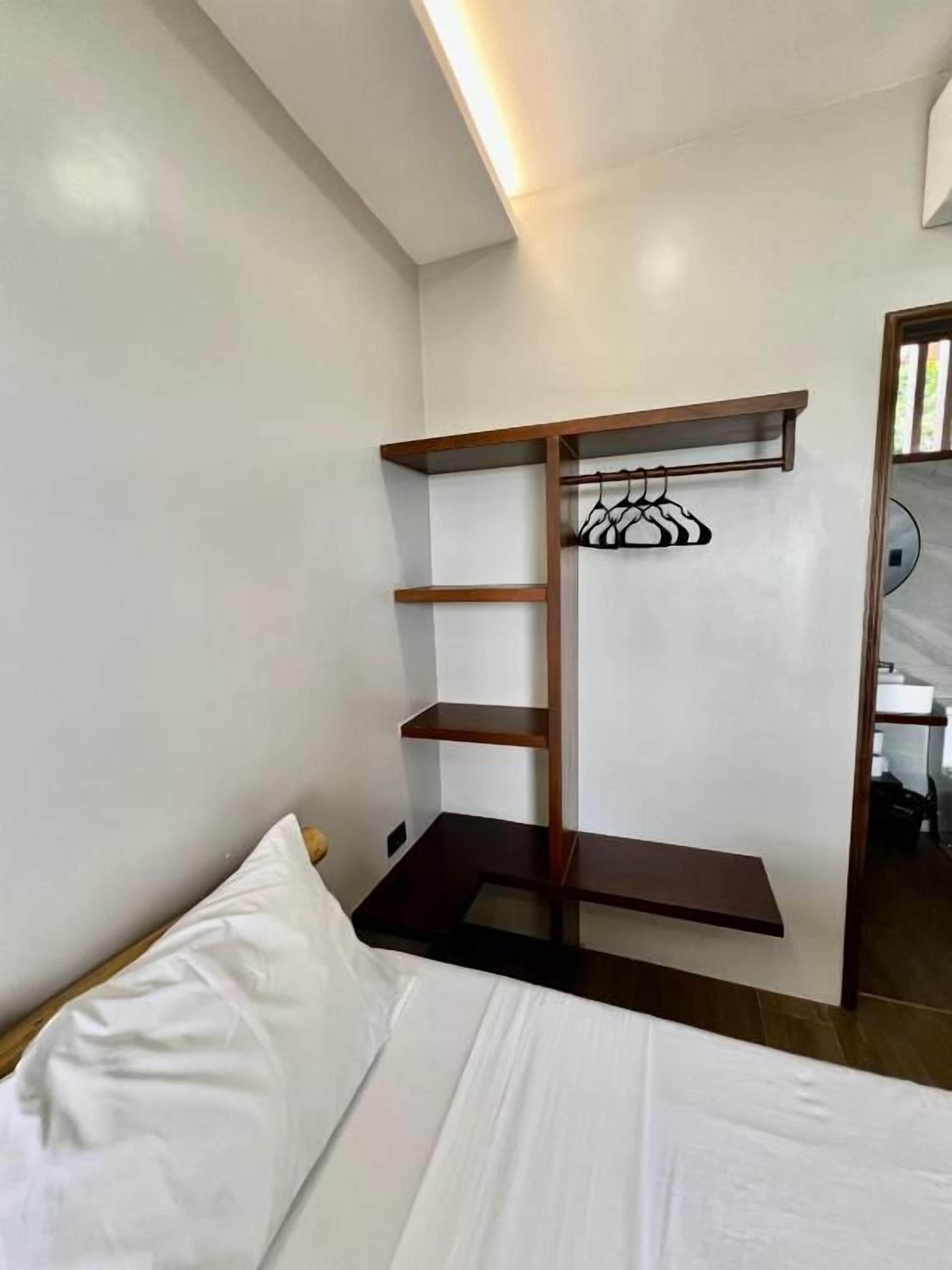 Quarto com cama, guarda-roupa de madeira com prateleiras e um cabideiro.