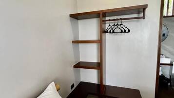 Quarto com cama, guarda-roupa de madeira com prateleiras e um cabideiro.