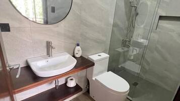 Un baño moderno con un espejo redondo, un lavabo, un inodoro y una ducha con mampara de vidrio.