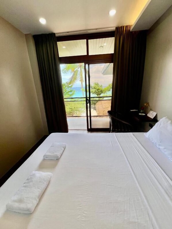 A hotel room with a bed, a nightstand, and a view of the ocean through a sliding door.