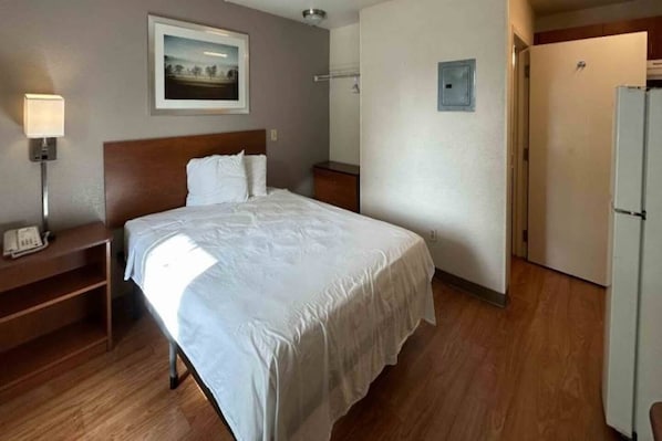 A hotel room with a bed, bedside table, lamp, and a door leading to a bathroom.