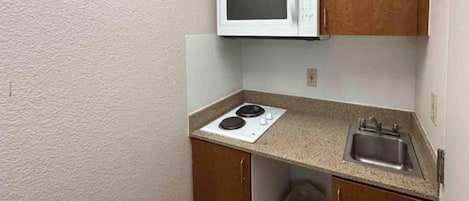 Una kitchenette compacta con microondas, estufa, pileta y basurero.