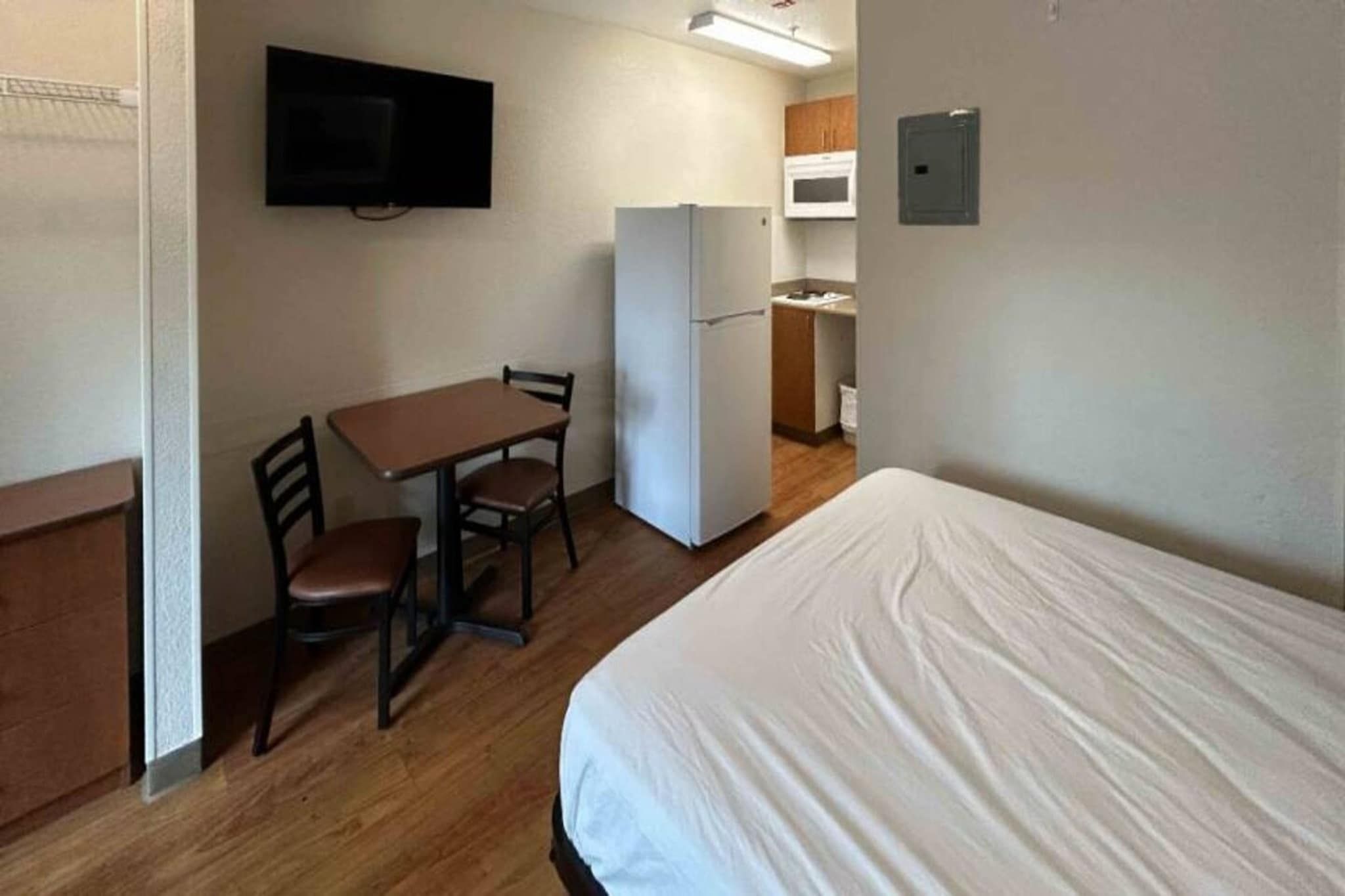 Quarto com cama, mesa para duas pessoas, geladeira, micro-ondas e pequena área de cozinha.