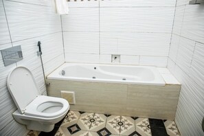 Et badeværelse med toilet, badekar og gulvfliser med mønster.