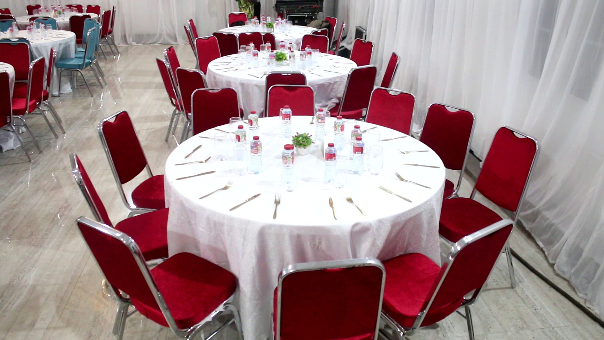 A banquet hall with round tables, red chairs, and white tablecloths.